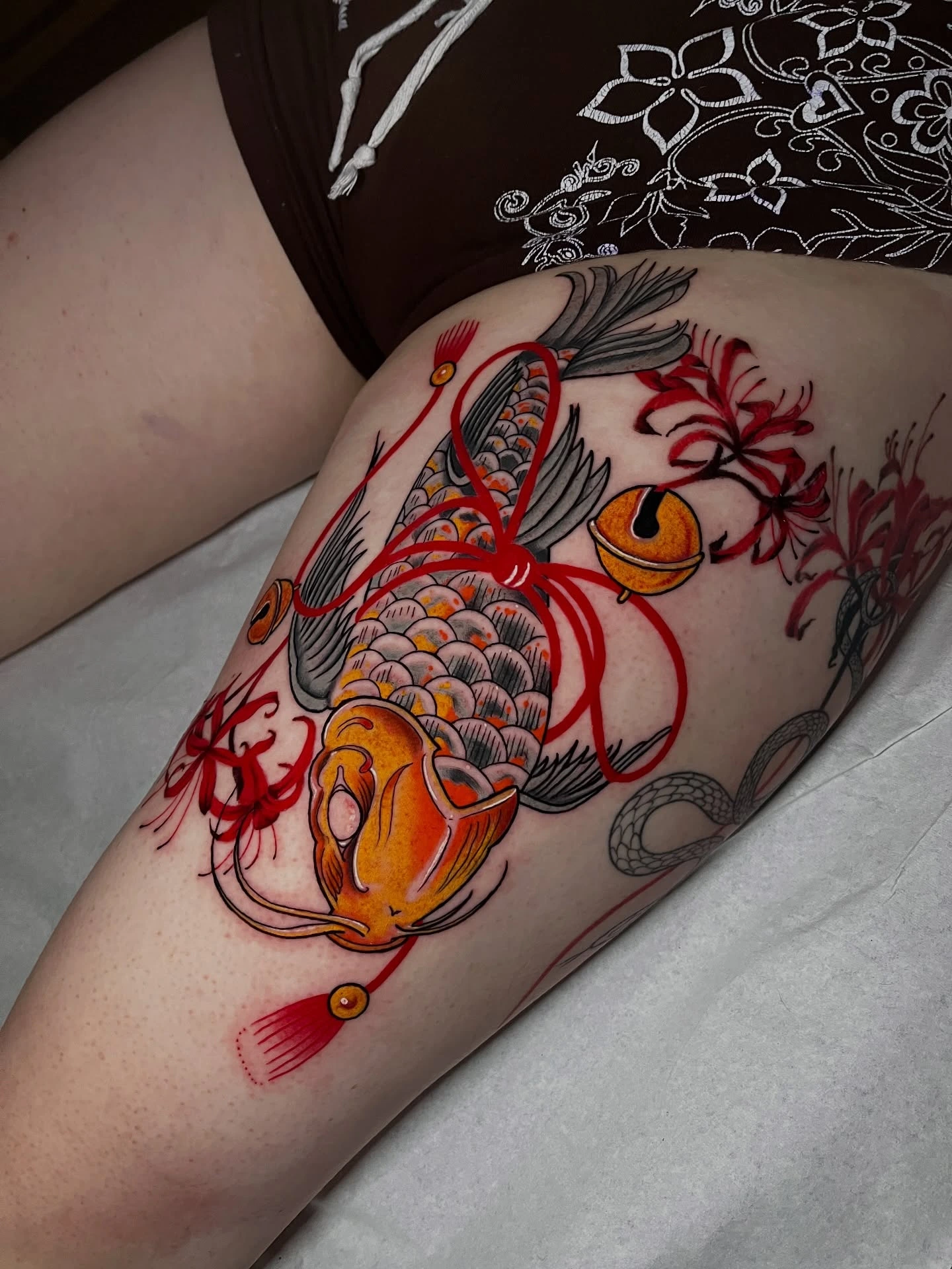 Koi fish wrapped in red ribbon with orange bell, spider lilies and snake